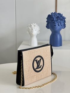 a purse sitting on top of a white table next to a vase with flowers in it