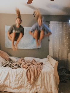 two children are jumping from a bed in a bedroom with white sheets and blankets on it