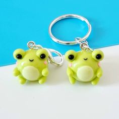 two green frog keychains with black eyes and one has a pink bow on it's head