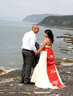 a man and woman standing next to each other near the ocean on a rocky shore