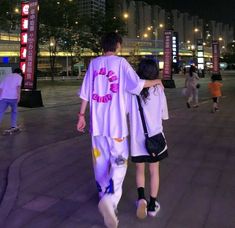 two people are walking down the street at night with their arms around each other,