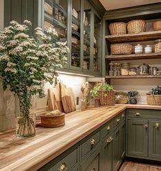 a kitchen filled with lots of green cabinets and wooden counter tops next to a vase full of flowers