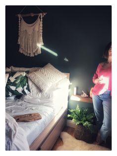 a woman standing in front of a bed next to a night stand with a lamp on it