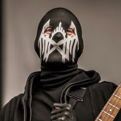 a man wearing a black and white mask holding a guitar in his right hand with the other hand on his hip