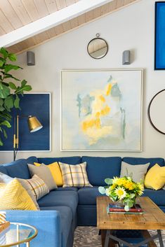 a living room with blue couches, yellow pillows and a painting on the wall