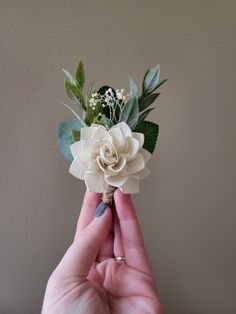 a hand holding a fake flower in it's right hand with greenery on top