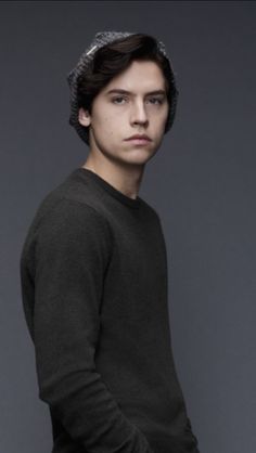 a young man wearing a knitted hat poses for a photo in front of a gray background