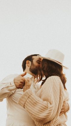 a man with long hair wearing a white hat and sweater kissing another man's forehead