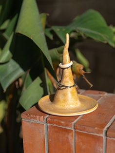 a small gold bell on top of a red brick wall next to green plants and leaves