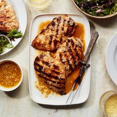 grilled chicken on a plate next to bowls of salad and condiments with dressing