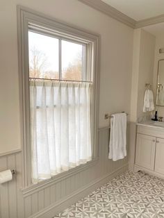 a bathroom with a large window, sink and shower curtained in valances