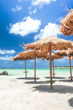 several straw umbrellas on the beach with blue sky and white clouds in the background