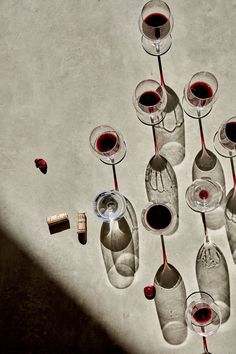 several wine glasses with red wine in them are lined up on the floor next to bottles and corks