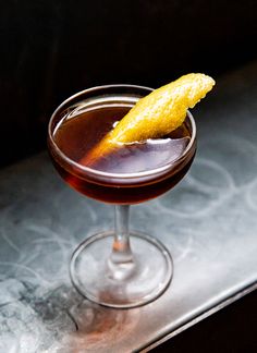 a close up of a drink in a glass with a lemon peel on the rim