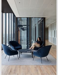 a woman sitting on a chair in a room with wooden floors and large glass windows