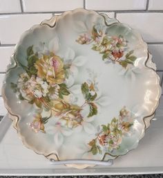 a white and gold plate with flowers on it sitting on a counter top next to a brick wall