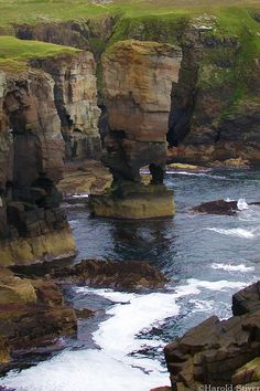 an ocean cliff with some rocks in the water