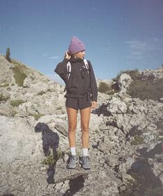 a woman standing on top of a rocky hill wearing a purple hat and black jacket