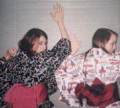 two women sitting on the floor with their arms in the air and one holding her hand up