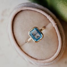 an engagement ring with a blue topaz sits in a velvet box on a table