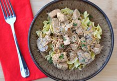 a bowl filled with pasta and meat on top of a red napkin next to a fork