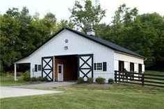 a white barn with black trim on the doors and windows is surrounded by green grass