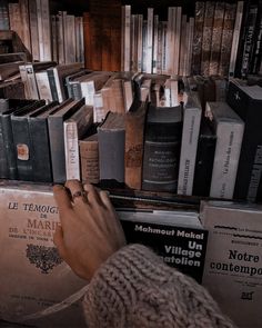 a person reaching for books on a book shelf in front of a pile of books