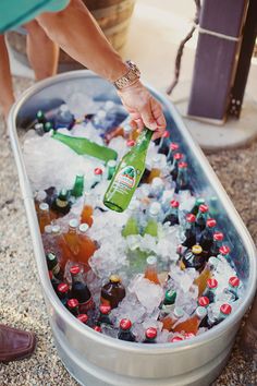 a person holding a beer bottle in a cooler filled with ice and soda bottles on the ground