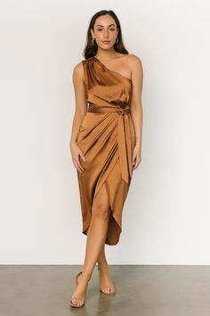 a woman wearing a brown dress with one shoulder draped over her body and sandals on the side