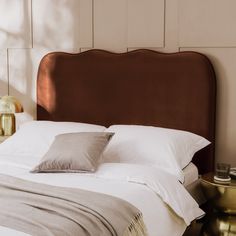 a bed with white sheets and brown headboard