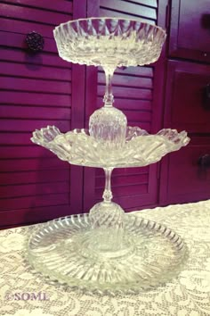 three tiered glass cake plate on top of a lace tablecloth with red shutters in the background