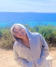 a smiling woman in a gray hoodie standing next to the ocean