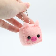 a hand holding a tiny pink pig keychain on a silver ball chain with black eyes