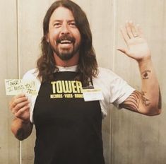 a man with long hair wearing an apron and holding two tickets in front of him