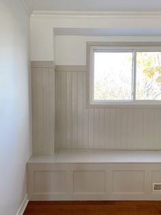 empty white room with wooden paneling and bench in the corner, looking out window