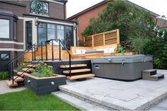 a hot tub sitting on top of a patio next to a lush green yard with stairs