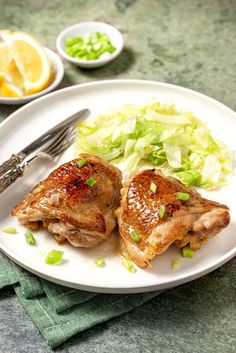 two pieces of chicken on a white plate with green salad and silverware next to it