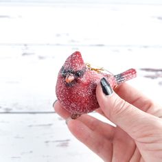 a hand holding a red bird ornament in it's right hand on a white wooden surface