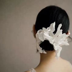 the back of a woman's head with white flowers in her hair and behind her is a gray wall