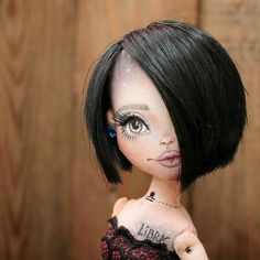 a doll with black hair and tattoos on it's face is posed in front of a wooden wall