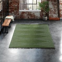 a room with a brick wall and green rug on the floor next to a wooden bench