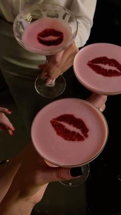 three people holding wine glasses with red liquid in the shape of lips on them,