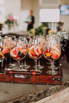 wine glasses filled with different types of fruit on a wooden tray in front of a stone counter