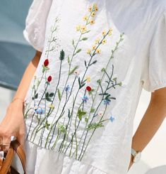 a woman is holding a purse and wearing a white shirt with colorful flowers on it