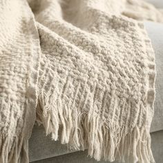 a close up of a blanket on a bed with white linens and fringed edges