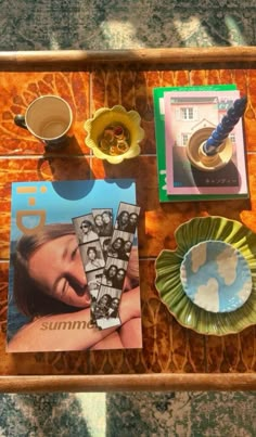 a table topped with plates and pictures on top of a wooden tray next to cups