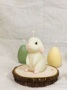 a small white toy sitting on top of a tree stump next to two green and yellow eggs