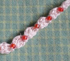 a crochet pattern with red beads is shown on a green surface and there are two pieces of yarn next to it