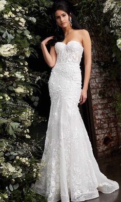 a woman in a white wedding dress standing next to flowers and greenery with her hand on her hip