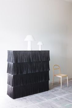 a chair sitting next to a black table with two lamps on it and a lamp shade